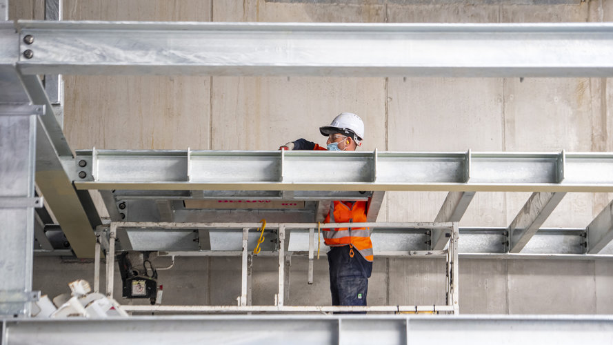 A construction worker is standing between steel beams while installing them at Waterloo Station. 