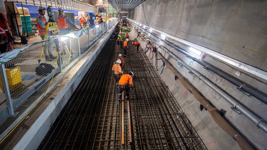 Several construction workers are working on the tracks inside Victoria Cross station.