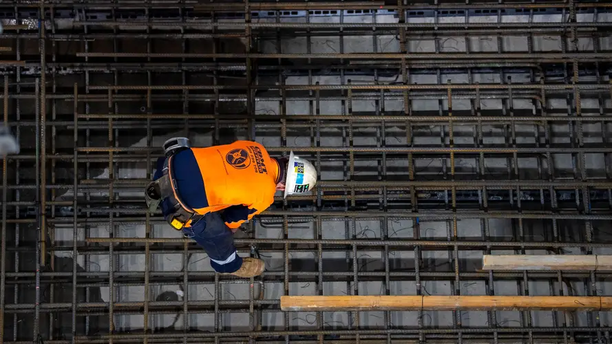 A construction worker bends over using a hand drill on the metal track supports inside Sydney Metro's Victoria Cross station.