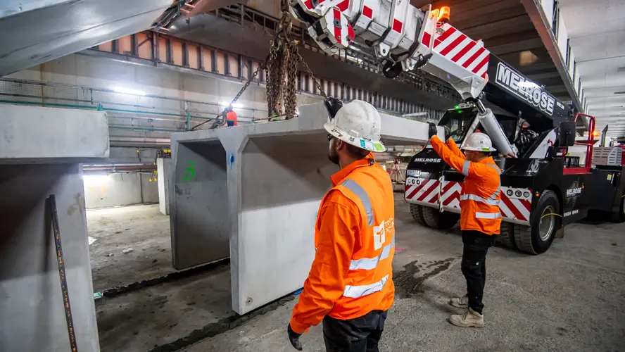 Two construction workers watching a concrete slab being craned into place.