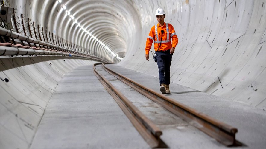 Man in high-vis walking through tunnel with tracks recently layed down.