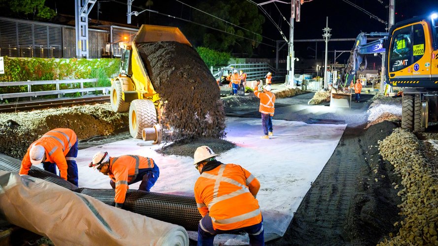 Truck emptying dirt and construction workers laying track at Sydney Metro's Chatswood Station.