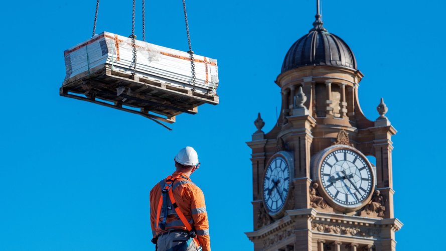 Low angle shot of construction worker viewing solar panels being lifted by a crane with the Central Station clock tower in the background