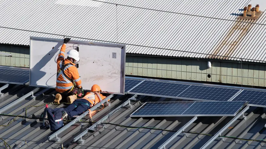 Two construction workers installing solar panels on Central Station's rooftop