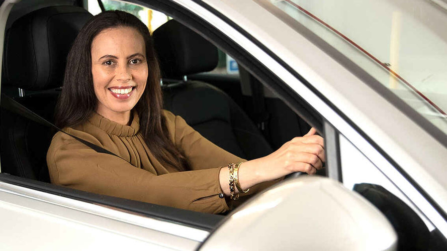 a women in brown coloured blouse is sitting in the driving seat with a smile on her face