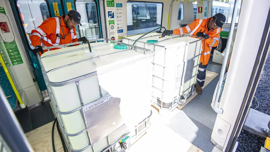 two workers are installing huge water bottles to simulate a full load of passengers as part of on-track testing 