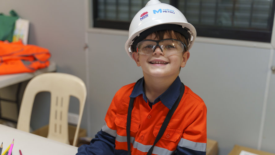 A young boy smiling in tradie's work wear with coloured pencil 