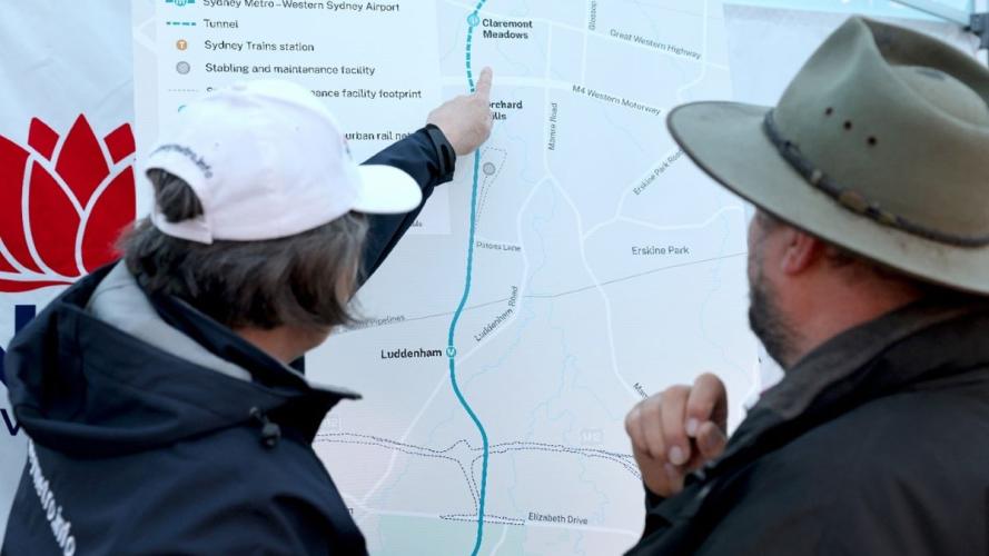 Two people standing in front of a Sydney Metro map with one person pointing at one of the stops 